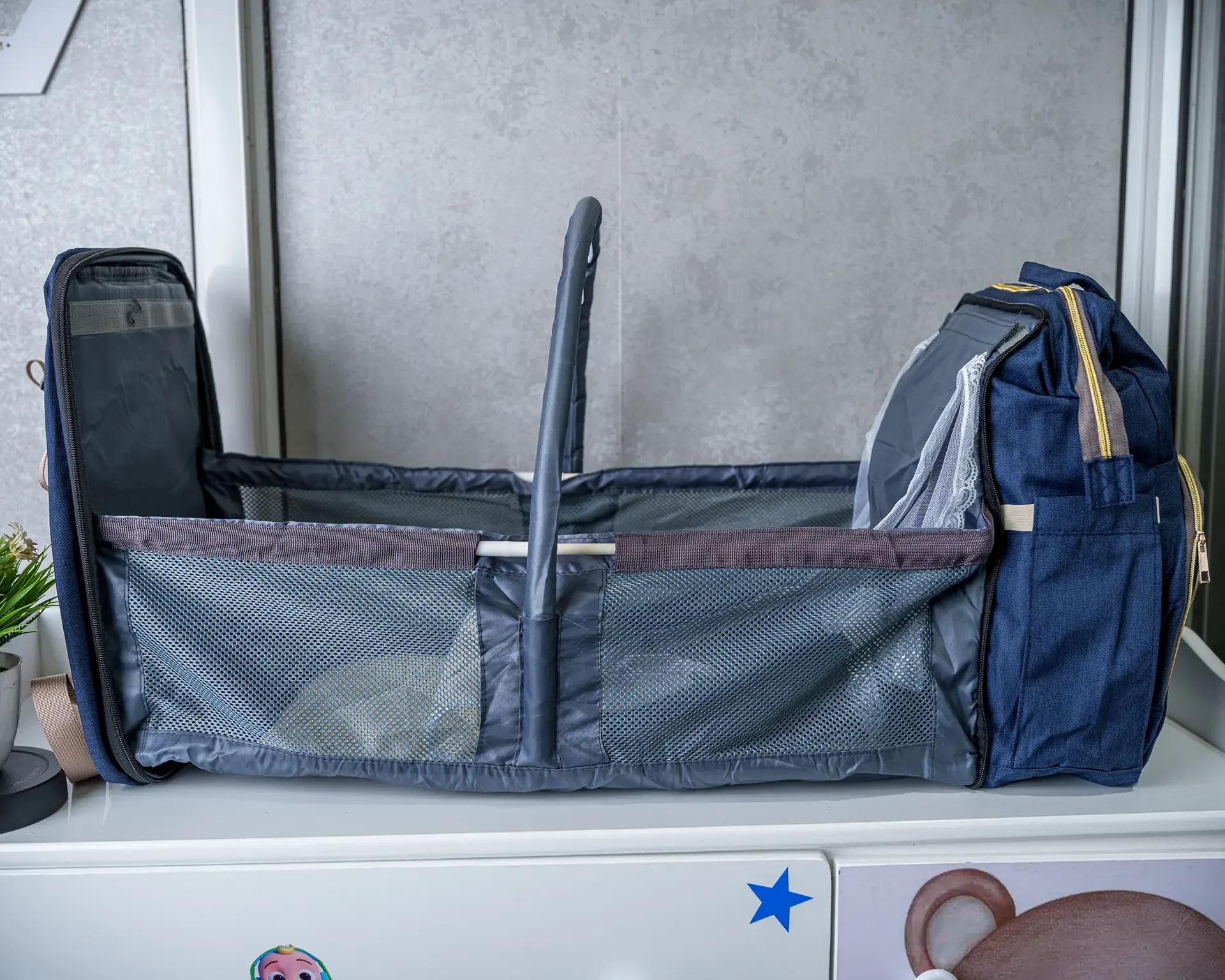 Foldable 2-in-1 diaper backpack opened into a portable baby bed with mesh sides, adjustable canopy support, and multiple storage compartments.