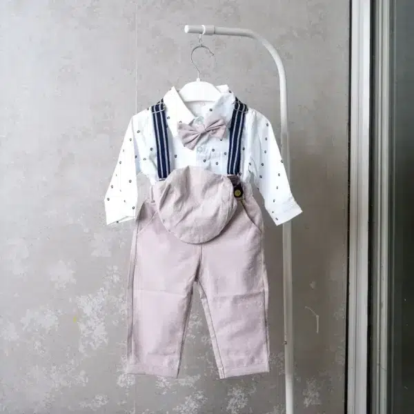Infant boy’s formal outfit featuring white long-sleeve printed shirt, blush pink pants with suspenders, bow tie, and matching cap.