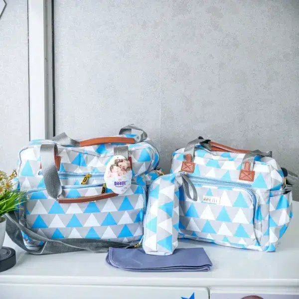 A set of blue and white geometric patterned diaper bags with gray and brown straps, including two bags, a bottle holder, and a changing mat, neatly arranged on a table.
