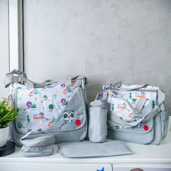 A five-piece diaper bag set displayed on a white surface, featuring two light gray bags with colorful cartoon animal prints, a matching bottle holder, a small pouch, and a foldable changing mat.
