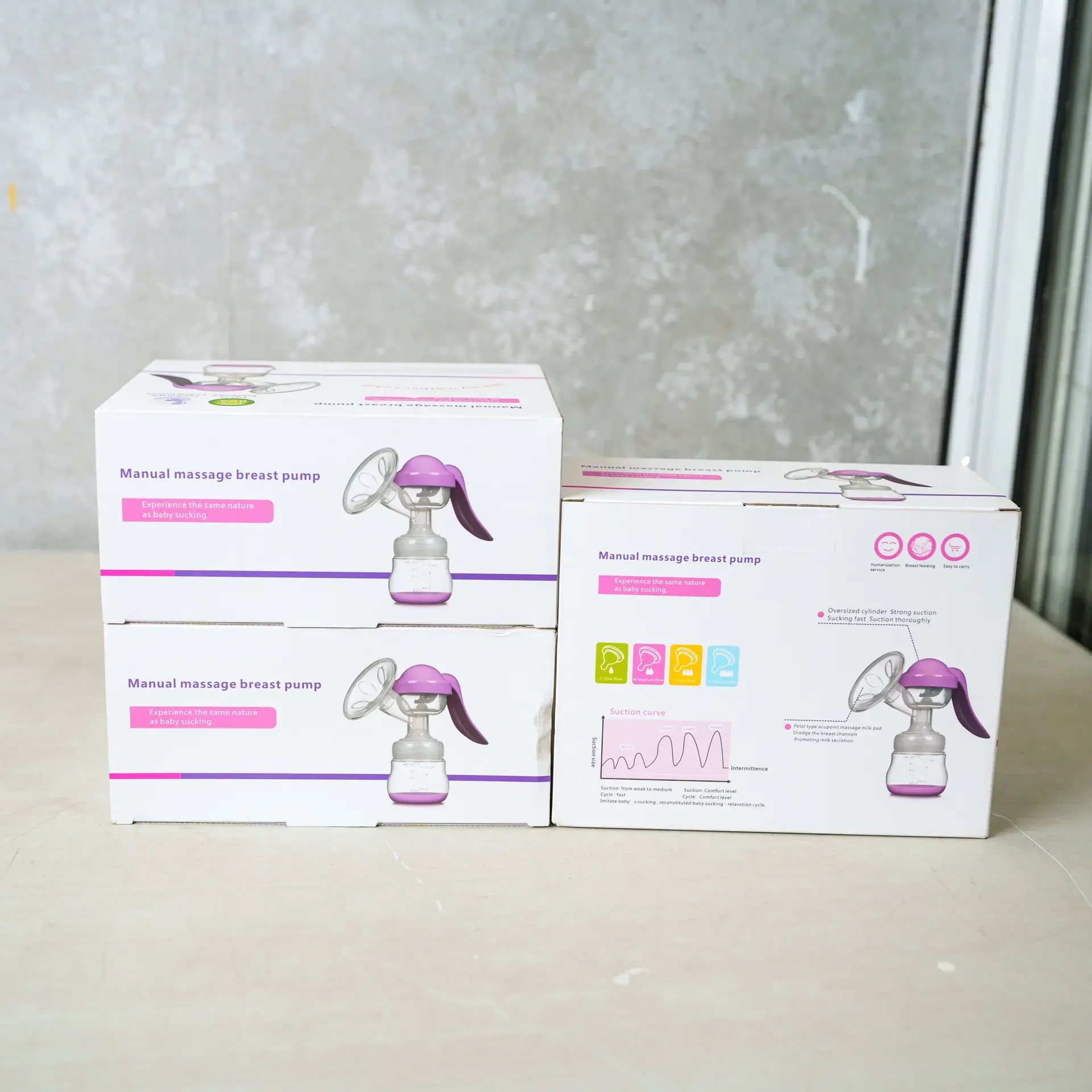 Stacked boxes of "Manual Massage Breast Pump" in white and purple packaging, showcasing the product's features such as strong suction, comfortable handle, and adjustable suction curve. Diagrams and icons on the side display its ergonomic design and user-friendly features.