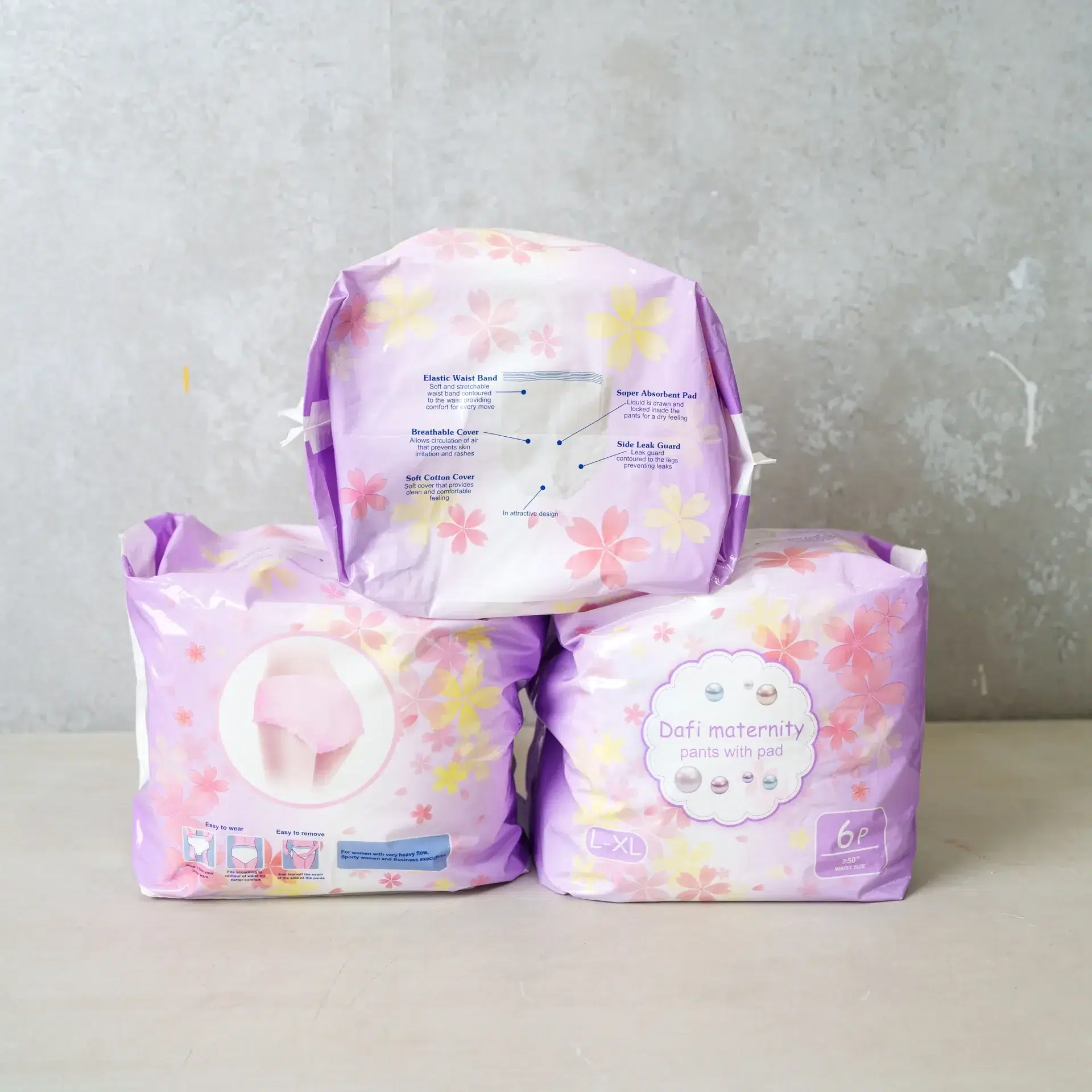 Three packs of "Dafi Maternity Pants with Pad" in soft purple packaging decorated with pink and yellow floral designs. One pack is displayed with a diagram highlighting features like the elastic waist band, super absorbent pad, side leak guard, breathable cover, and soft cotton cover.
