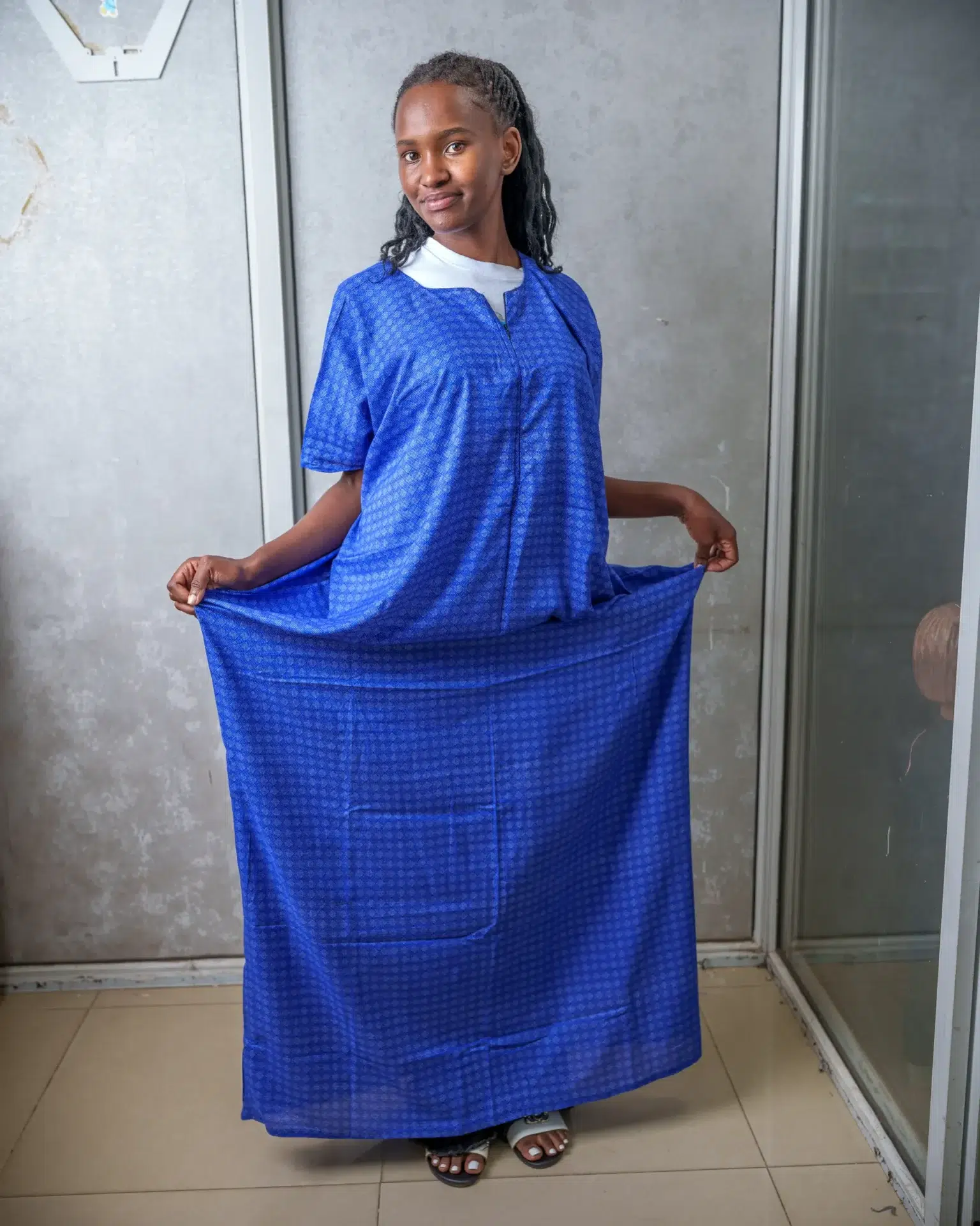 Woman wearing a blue nursing dera with subtle geometric print, holding the sides to show the loose fit and full-length design.