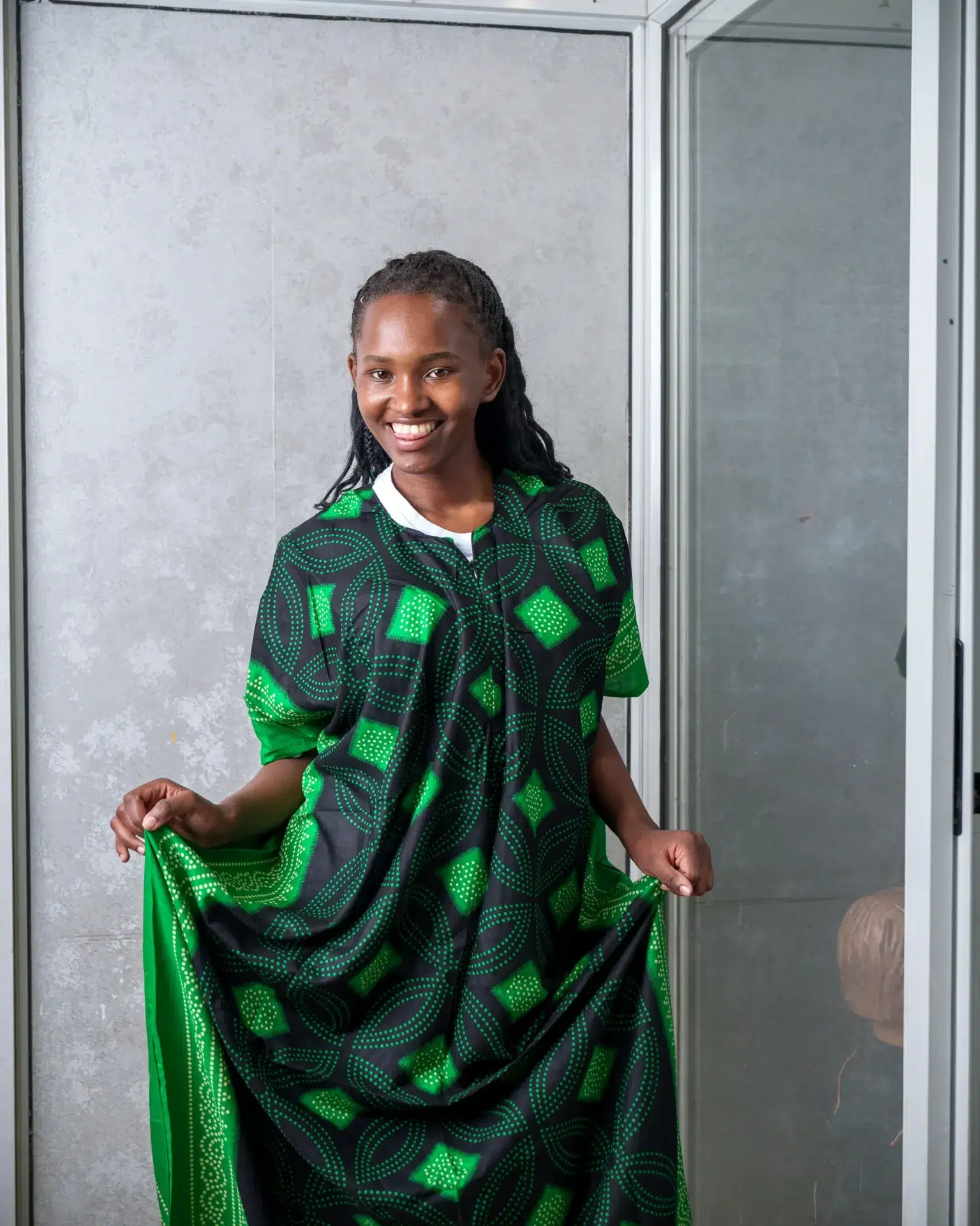Woman dressed in a black nursing dera with green African-inspired patterns, smiling and displaying the wide, flowing cut of the outfit.